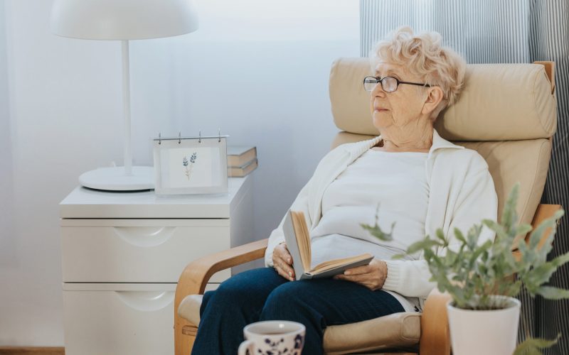 Pensive elderly lady sitting with a book in an armchair in a nursing home